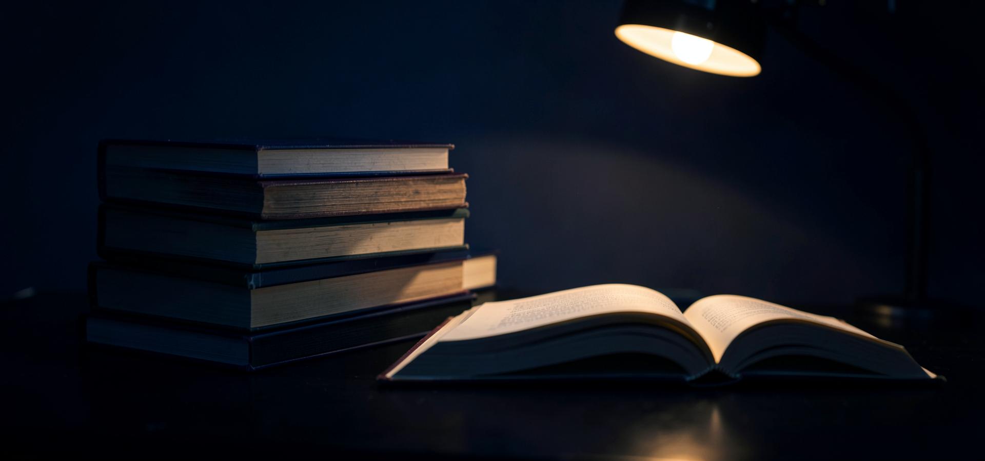 Livros empilhados e um livro aberto sob luz de luminária